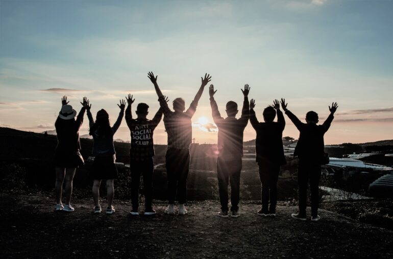 En grupp människor sträcker upp armarna i luften, de står vända mot solnedgång