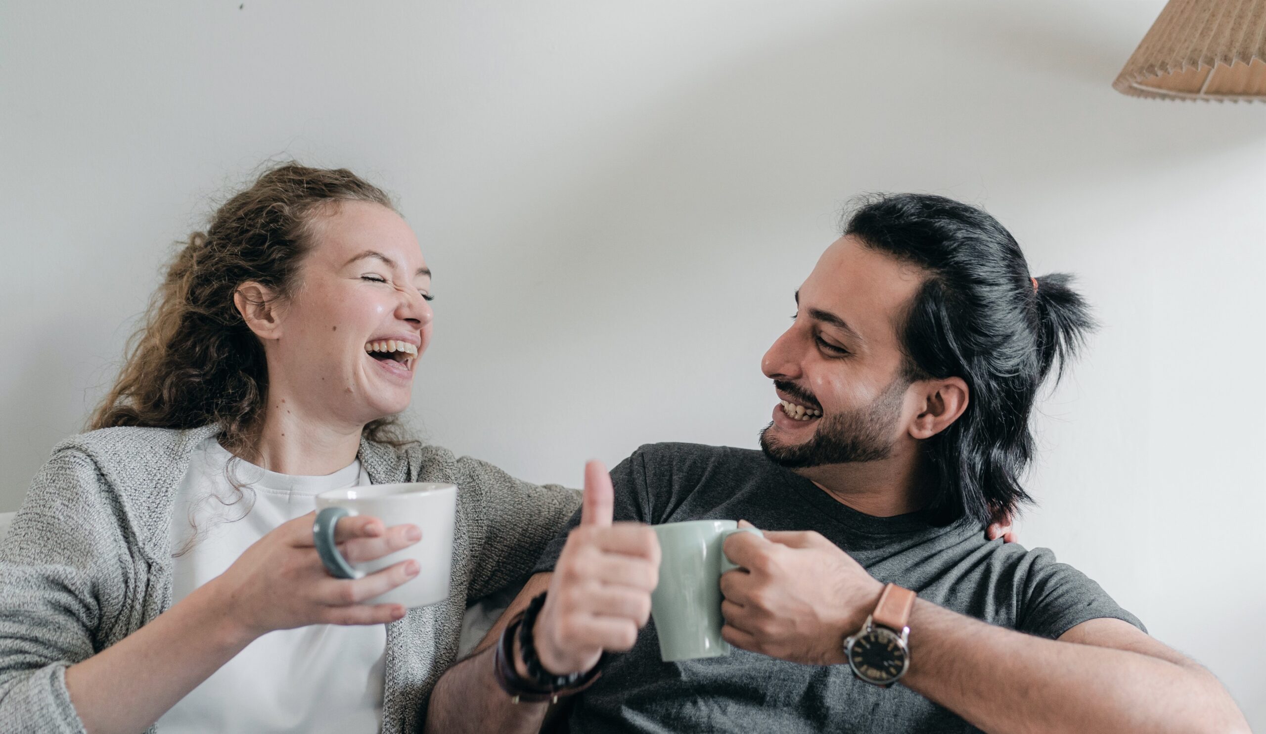 Ett glatt par som sitter i en soffa och dricker kaffe