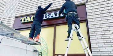 Hantverkare som monterar skyltar på en fasad.