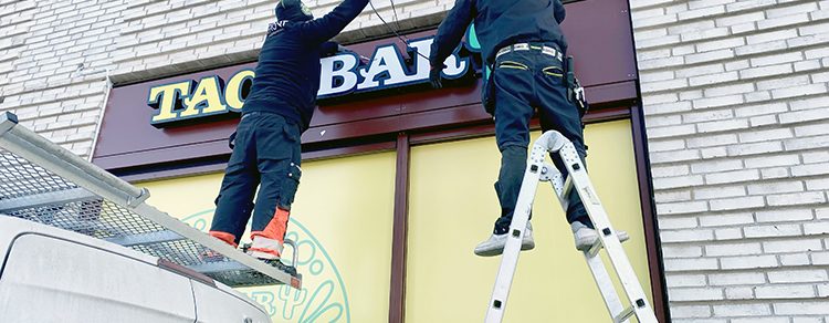 Hantverkare som monterar skyltar på en fasad.