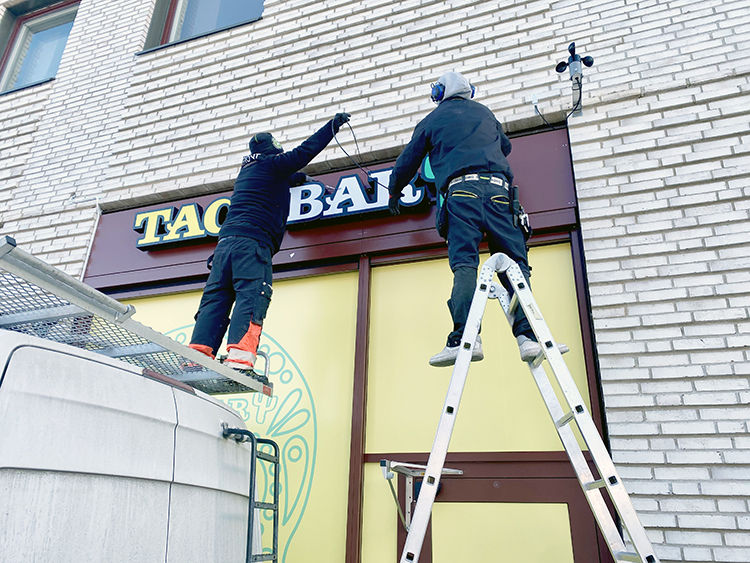 Hantverkare som monterar skyltar på en fasad.