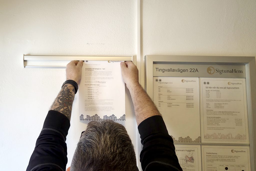 Dick passar på att hänga upp en avisering i trapphuset.